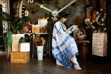 Traveler thai young women wear indigo tie dye paint shawl and scarf posing portrait sit read magazine book for take photo with decorate furniture at coffee shop on June 21, 2020 in Bangkok, Thailand