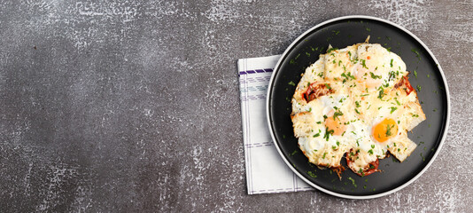 Fried eggs with bread, tomatoes and cheese on a round plate on a dark background. Top view, flat lay
