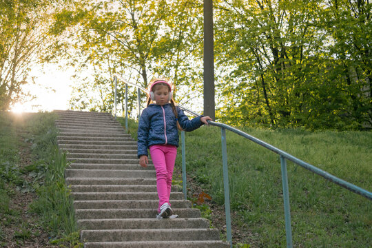 A little girl in headphones goes down the steps in an autumn park. A child listens to music while walking in the park.