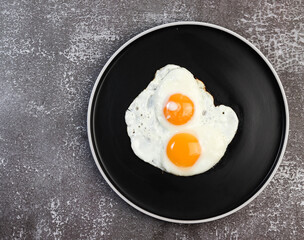 Fried eggs on on a round plate on a dark background. Top view, flat lay