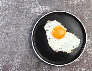 Fried egg on on a round plate on a dark background. Top view, flat lay