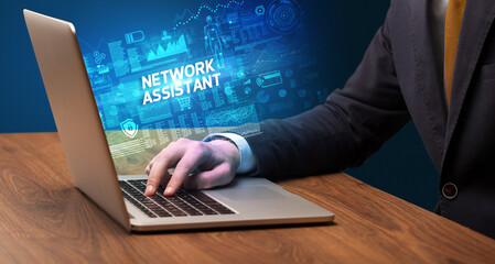 Businessman working on laptop with NETWORK ASSISTANT inscription, cyber technology concept