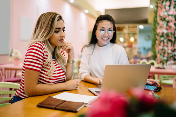 Diverse freelancers watching education webinar during online courses using cafe wifi connection for web browsing on modern laptop computer, skilled women reading network news while installing app
