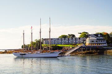 Luxurious and elegant Victorian architecture New England wooden cottage resort or hotel in Bar Harbor, Maine with beautiful sailing yacht or windjammer on sunny morning