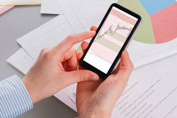 Businesswoman working with financial investment using smartphone. Woman trader looking on smartphone with graphs analysis. Accounting, economic, commerce concept.