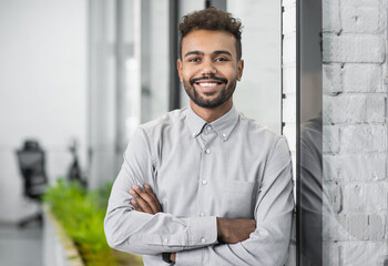Handsome young businessman with folded arms in the office. Cheerful self confident men with crossed hands portrait. Business success concept