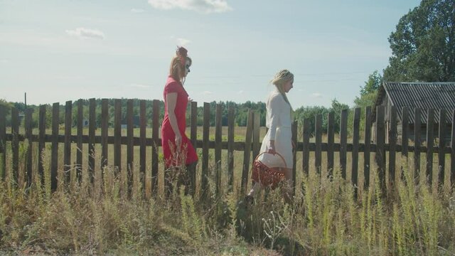 Joyful positive young women with candy baskets in halloween make-ups, dressed as santa muerte and drowned woman, walking in village , trick or treating on halloween holiday in countryside.