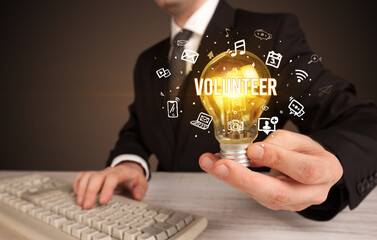 Businessman holding light bulb with VOLUNTEER inscription, social media concept