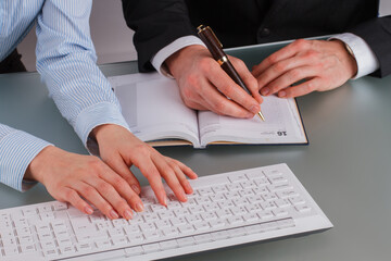 Fototapeta premium Business man and business woman working at office. Man making a note while woman using computer. Close up of business people discussing business plan.