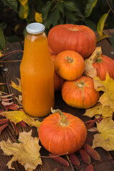Ripe pumpkin fruits, autumn leaves and a bottle of pumpkin juice on a wooden table.