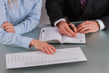 Hands of man and woman working together in office. Two colleagues discussing data with computer and paper notebook.