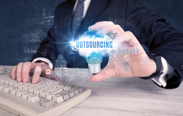 Businessman holding a light bulb with OUTSOURCING inscription, new business concept