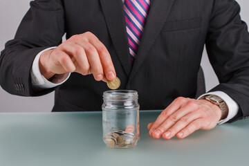 Hands of businessman puts coins in glass jar. Budget planning. Saving money concept.