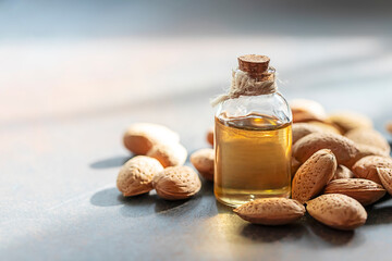 Glass bottle of almond oil and almonds on a dark background.