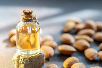 Glass bottle of almond oil and almonds on a dark background.