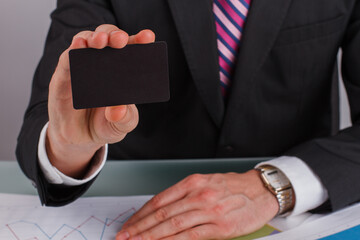 Close up businessman hand showing business card. Businessman sitting at table with documents and holding empty business card.