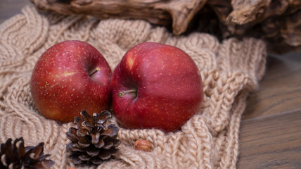 Autumn still life with apples and nuts. Autumn background with apples on a warm knitted scarf, a wooden plate, autumn leaves, hazelnuts and cones.