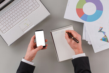 Businessman using phone and writing in notebook. Man accountant working at office. Economic profit concept.