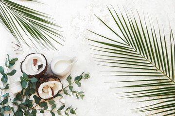 Natural and organic spa still life ingredients with fresh coconut, moisturizer cream and collection of different green leaves on rustic white surface. Top view, blank space