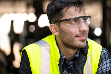 Engineer or technician wearing safety glasses and vest sitting on the floor and relax in the metalworking factory. He is looking away. Relaxation and industrial concept.