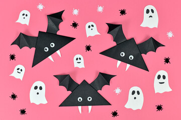 Black paper vampire bats with funny googly eyes and and ghosts and spider shaped confetti on pink Halloween background 