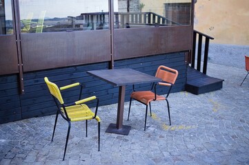 Fototapeta na wymiar A wooden table on the street with yellow and orange chairs (Corinaldo, Marche, Italy, Europe)