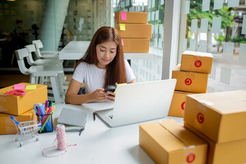 Closeup Asian smile Woman are receiving orders via cell phone and holding hand near laptop. Small business entrepreneur SME working with box at home, SME e-commerce digital technology concept.