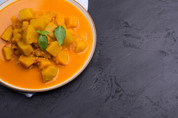 Curry or pumpkin soup served in a ceramic platter on a black background - top view with space for writing messages.
