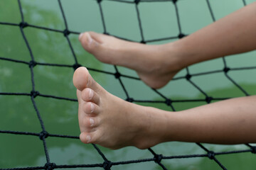 The little girl's legs slept on a net in a clear green body of water.