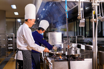 Asian male chef cooking food with his colleuge in the hotel kitchen