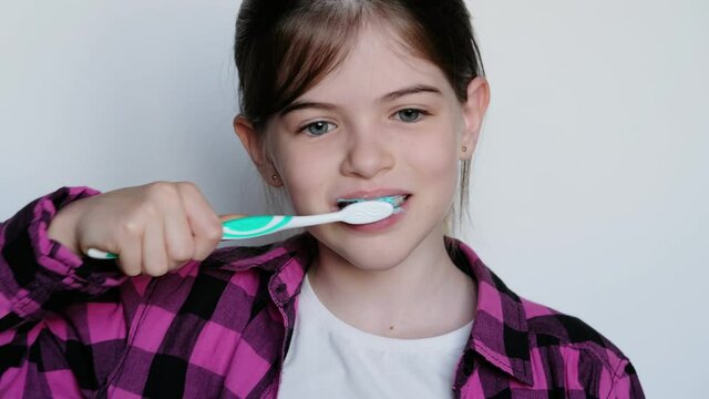little / young girl in a pink plaid shirt brushes her teeth on a white background