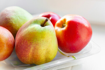 Close-up autumn fruits on a plate. Pears and apples are stacked in a plate on a light background. Selective soft focus. Healthy organic food. Natural products.