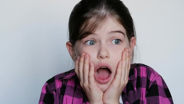 little / young girl in a pink plaid shirt with big blue eyes is surprised, opened her mouth in surprise. On white background.
