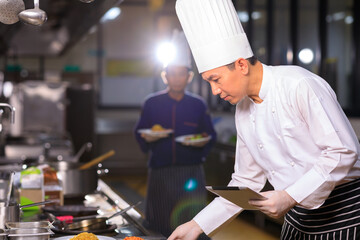 Asian male chef cooking food with his colleuge in the hotel kitchen