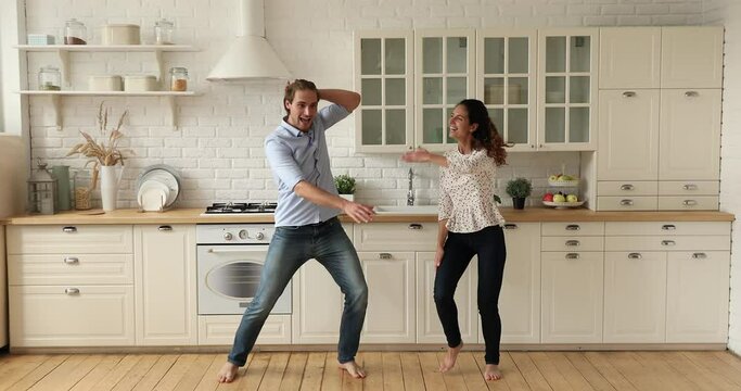 Full length couple dancing together in cozy spacious domestic kitchen while listen energetic music feels cheerful. Dating and relationships, happy home owners celebrate relocation at new house concept