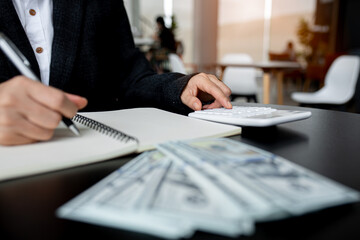 Closeup of business woman hands counting US dollar cash on the table.people holding Us dollar banknotes money ,using calculator calculate saving money with happy in office.