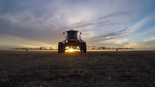 Sprayer Spraying Herbicide At The Post-harvest Fields On A Sunset. - ground level- wide shot