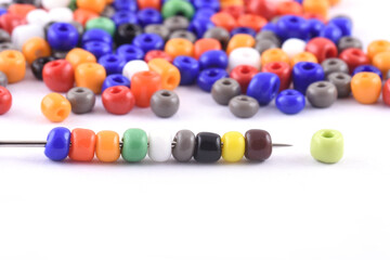 Multi colored Beads spread on white background with needle. Beads with needle . Close up,...