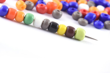 Multi colored Beads spread on white background with needle. Beads with needle . Close up,...