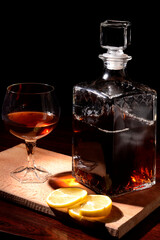 Glass of cognac with lemon on a wooden background. Sliced lemon and knife on a cutting board.