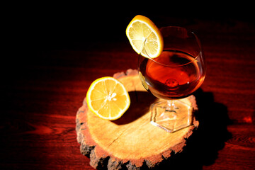 Glass of cognac with lemon on a wooden background. Sliced lemon and knife on a cutting board.
