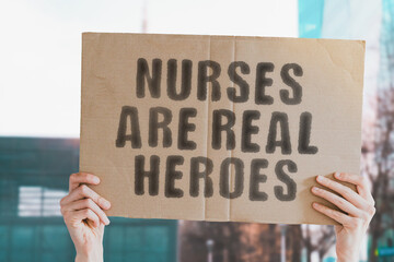 The phrase " Nurses are real heroes " on a banner in men's hand with blurred background. Superhero. Job. Responsibility. Hospital. Treatment. Help. Care. Profession