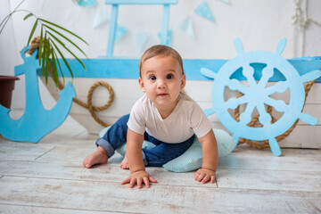 baby boy in white t-shirt and jeans sitting on a wooden boat background