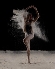 Fototapeta na wymiar Beautiful sensual fit slim dancer in black body with long blond hair throwing dust, flour, powder on black background.