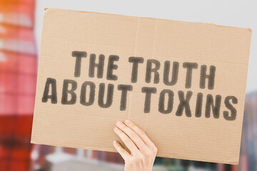 The phrase " The truth about toxins " on a banner in men's hand with blurred background. Poison. Polluted. Toxic. Dangerous. Hazardous. Healthcare