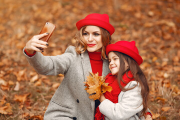 Fashionable mother with daughter. Family in a autumn park. Little girl in a red hat