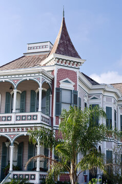 Vertical: Historic Queen Anne architecture house with upstair balconies, tower, multi color paint, wooden shutters, tall windows, slate shingle roof, palm trees
