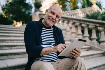 Cheerful senior male browsing tablet on stairs in park