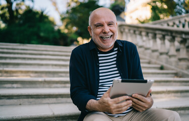 Fototapeta premium Laughing aged man using tablet on stairs in park