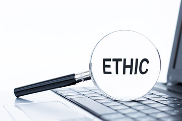 Ethic word text inscription written on a magnifying glass lying on the laptop keyboard. Ethics concept